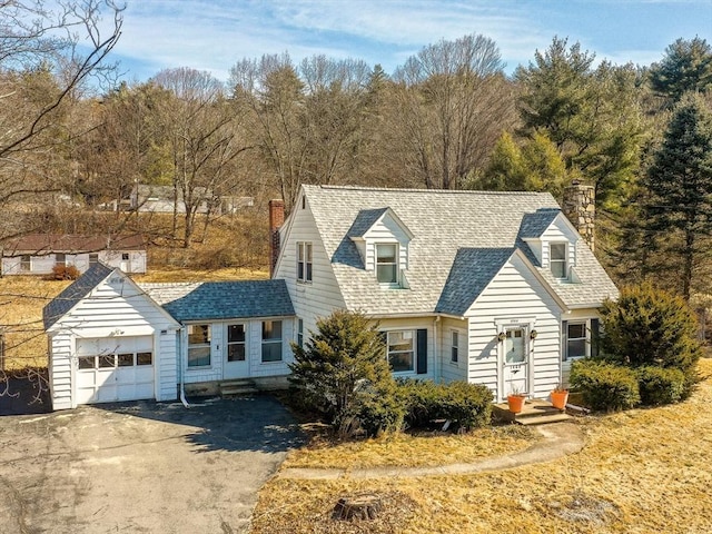 cape cod-style house featuring entry steps, a chimney, a garage, and a shingled roof