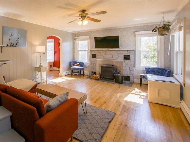 living area with a baseboard heating unit, crown molding, light wood-type flooring, arched walkways, and a ceiling fan