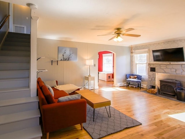 living area with stairway, a wood stove, wood finished floors, and ceiling fan