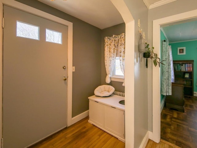 foyer featuring wood finished floors, baseboards, arched walkways, and ornamental molding