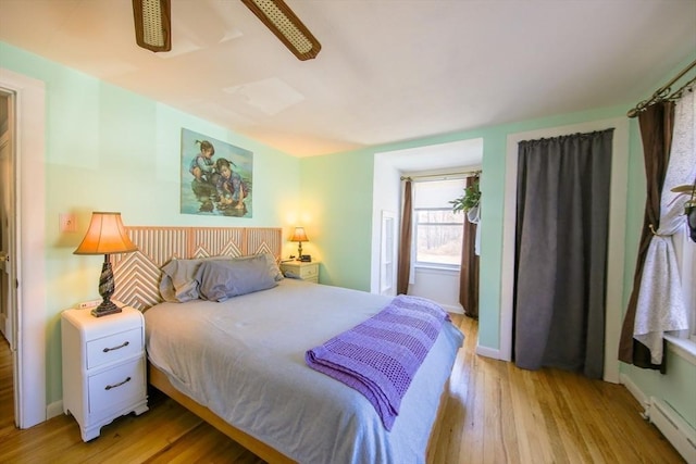 bedroom with a baseboard heating unit, light wood-style flooring, and baseboards