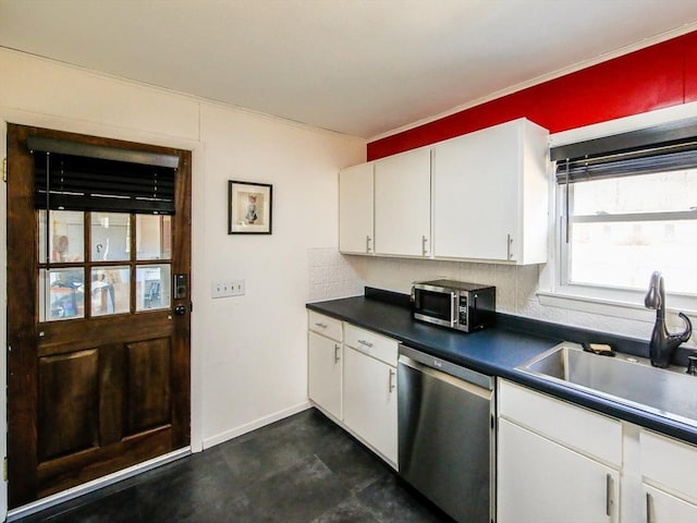 kitchen with a sink, dark countertops, appliances with stainless steel finishes, white cabinets, and baseboards