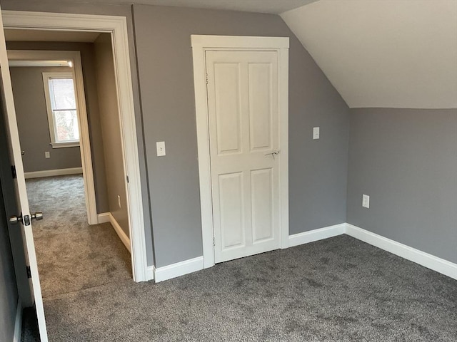 additional living space featuring dark carpet, lofted ceiling, and baseboards