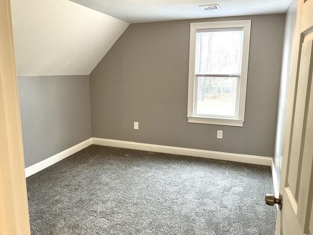 additional living space featuring dark colored carpet, visible vents, baseboards, and vaulted ceiling