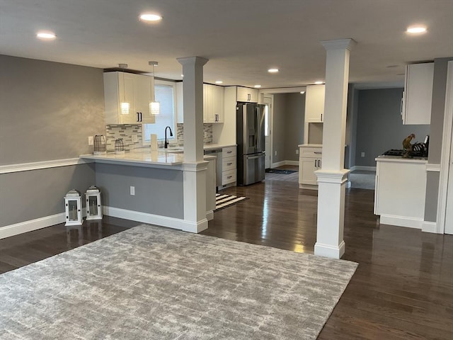 kitchen with a peninsula, decorative columns, a sink, light countertops, and stainless steel fridge