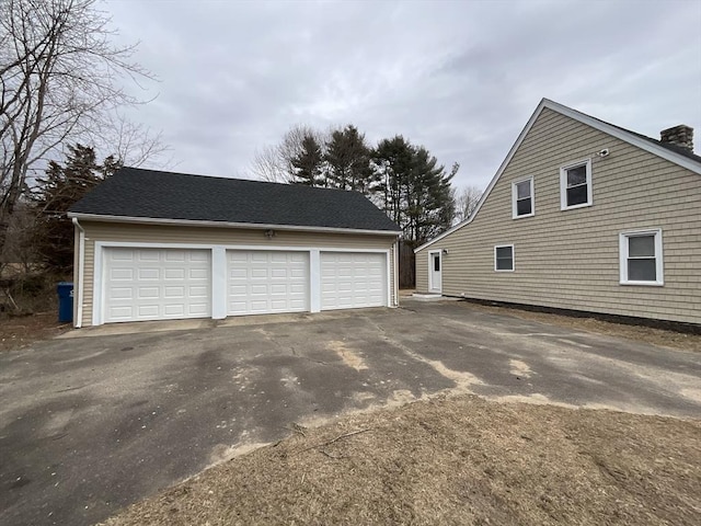 exterior space featuring an outbuilding, a shingled roof, and a garage