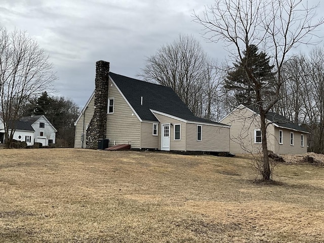 view of front facade featuring cooling unit, a chimney, a yard, and roof with shingles