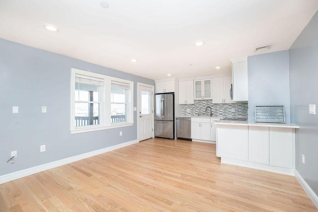 kitchen with kitchen peninsula, stainless steel appliances, light hardwood / wood-style floors, decorative backsplash, and white cabinets