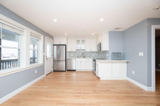 kitchen featuring white cabinetry, sink, backsplash, light hardwood / wood-style floors, and stainless steel appliances