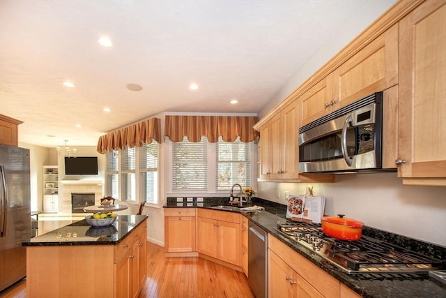 kitchen featuring a center island, dark stone counters, sink, appliances with stainless steel finishes, and light hardwood / wood-style floors