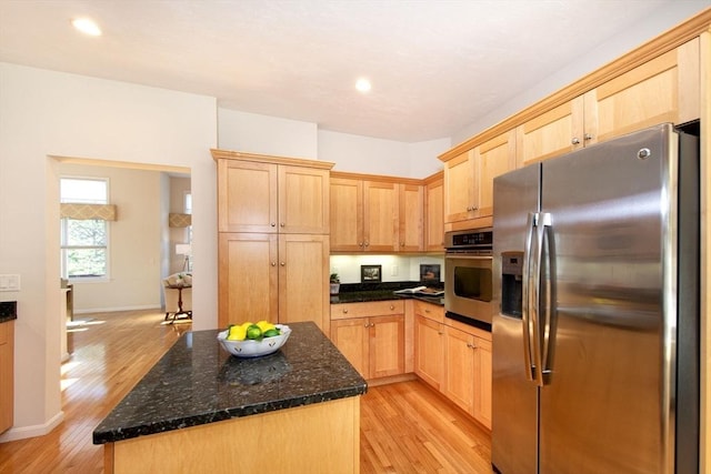 kitchen with light hardwood / wood-style floors, dark stone countertops, light brown cabinetry, and appliances with stainless steel finishes