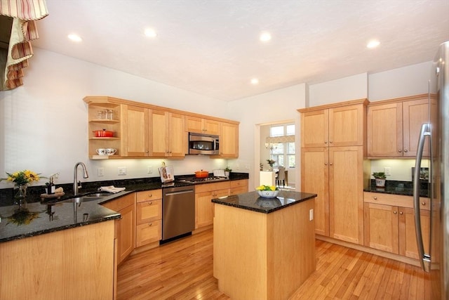 kitchen featuring appliances with stainless steel finishes, light hardwood / wood-style flooring, dark stone countertops, and sink