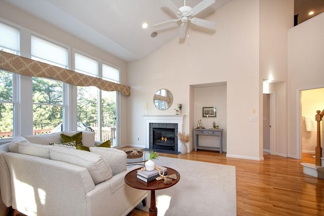 living room with a tile fireplace, light hardwood / wood-style floors, high vaulted ceiling, and ceiling fan