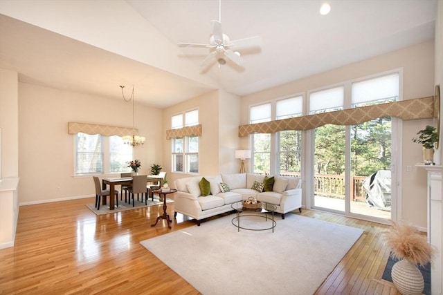 living room featuring ceiling fan with notable chandelier, light wood-type flooring, and high vaulted ceiling