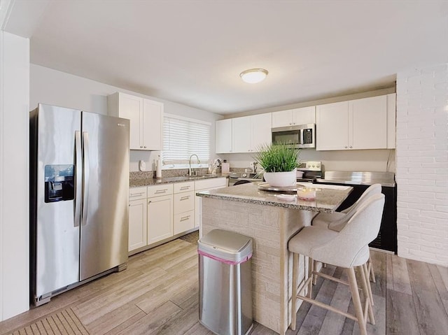 kitchen featuring white cabinetry, a kitchen bar, appliances with stainless steel finishes, and light wood finished floors