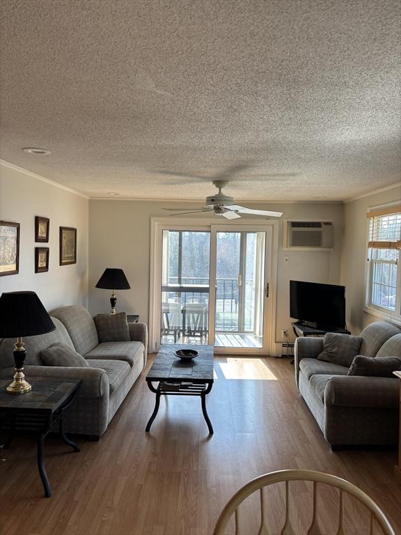 12 Candlewood Ln Unit 2-2, Dennis, MA 02639 - living room with a textured ceiling, a baseboard radiator, a ceiling fan, wood finished floors, and a wall mounted air conditioner