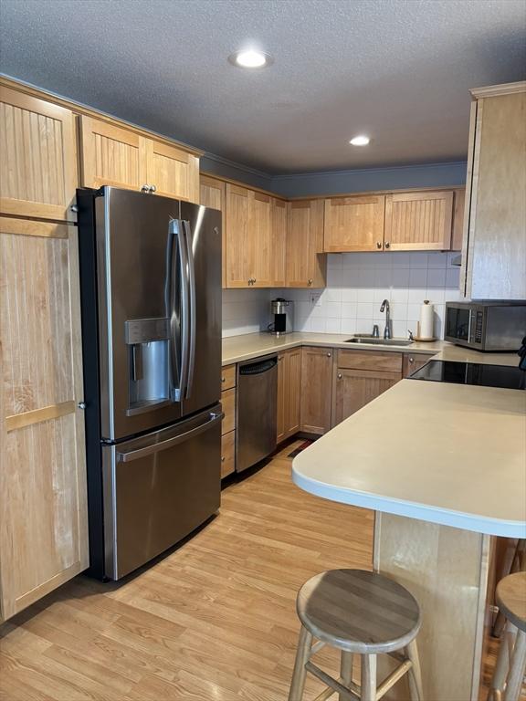 12 Candlewood Ln Unit 2-2, Dennis, MA 02639 - kitchen with a sink, stainless steel appliances, a breakfast bar, light wood-style flooring, and light countertops