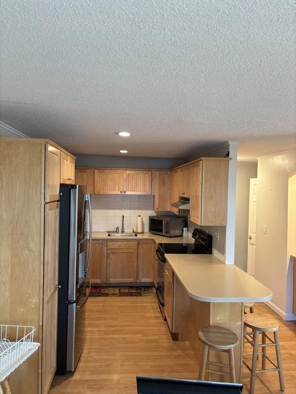 12 Candlewood Ln Unit 2-2, Dennis, MA 02639 - kitchen with a peninsula, appliances with stainless steel finishes, light wood finished floors, a sink, and a textured ceiling