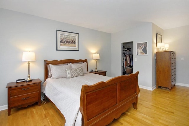 bedroom featuring a walk in closet, baseboards, a closet, and light wood finished floors