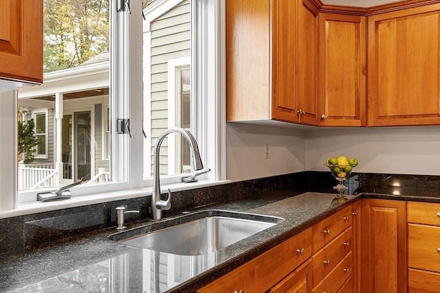 kitchen with a sink, brown cabinetry, and dark stone countertops