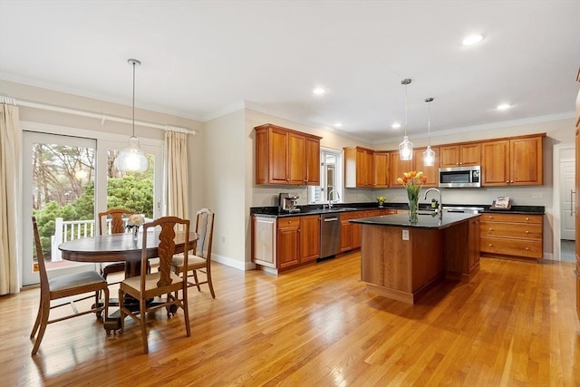 kitchen featuring dark countertops, brown cabinetry, an island with sink, stainless steel appliances, and light wood-type flooring