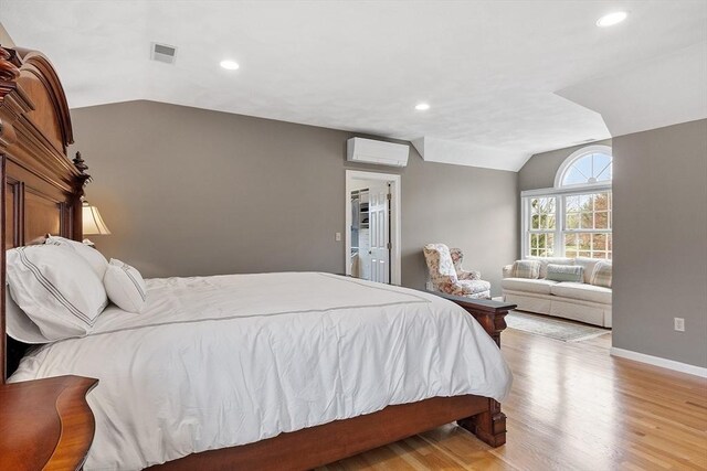 bedroom with visible vents, light wood-style floors, a wall mounted air conditioner, baseboards, and vaulted ceiling