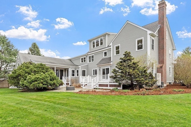 rear view of house with a lawn, a chimney, a shingled roof, and a deck