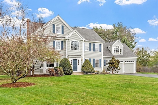 colonial home with driveway, a chimney, a front yard, and a garage