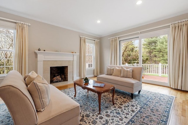 living area featuring light wood finished floors, recessed lighting, baseboards, a tile fireplace, and ornamental molding