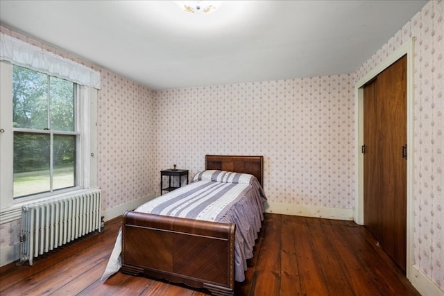 bedroom with multiple windows, a closet, dark hardwood / wood-style floors, and radiator heating unit