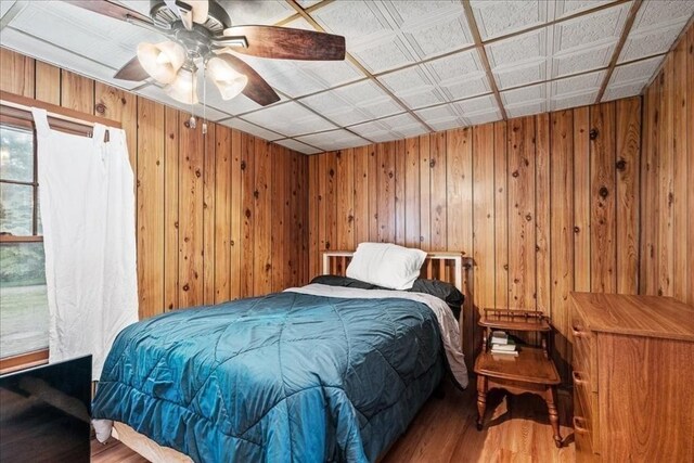 bedroom featuring light wood-type flooring, ceiling fan, and wooden walls