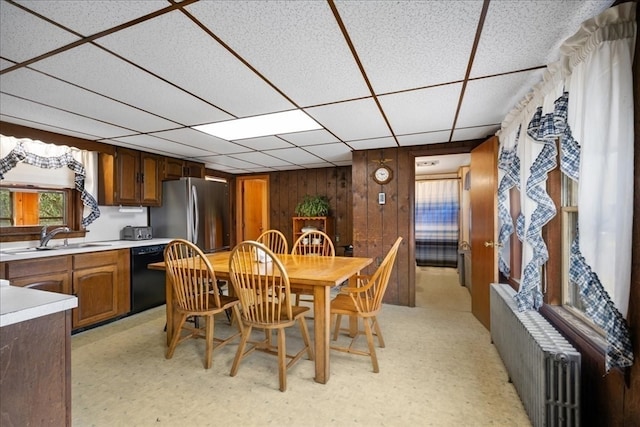 dining area featuring radiator heating unit, wooden walls, a drop ceiling, and sink