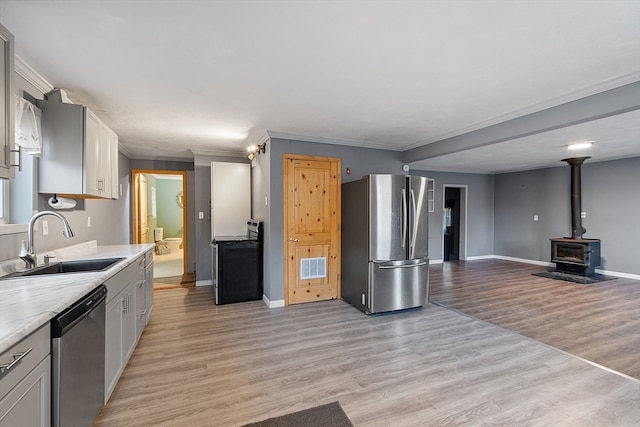 kitchen with crown molding, appliances with stainless steel finishes, a wood stove, sink, and light hardwood / wood-style flooring