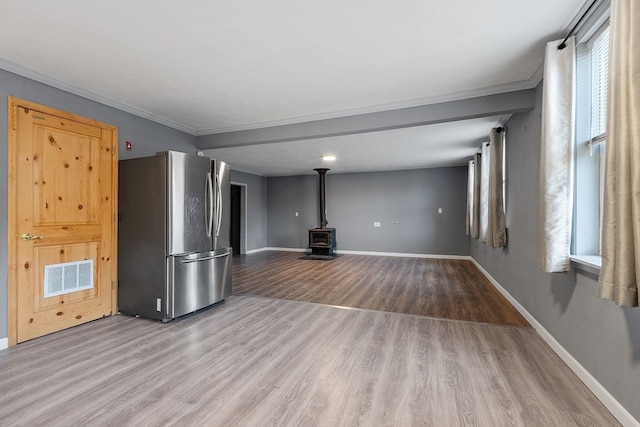 unfurnished living room featuring hardwood / wood-style floors, a wood stove, and ornamental molding