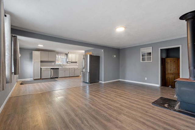 unfurnished living room featuring light wood-type flooring, a wood stove, and ornamental molding