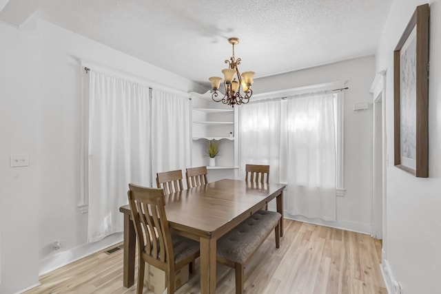 dining space with light wood-type flooring, a textured ceiling, and an inviting chandelier