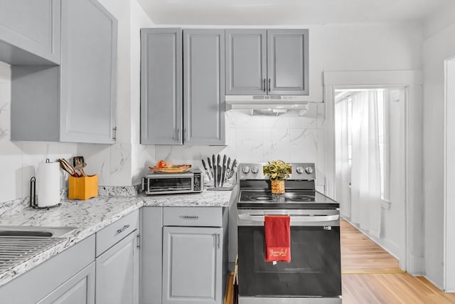 kitchen with stainless steel range with electric stovetop, gray cabinetry, tasteful backsplash, and light hardwood / wood-style flooring