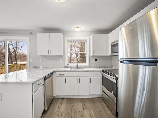 kitchen with light wood-style flooring, appliances with stainless steel finishes, a peninsula, white cabinetry, and a sink