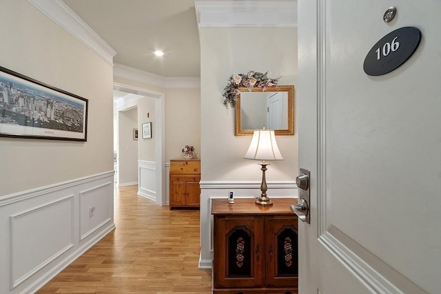 corridor featuring a decorative wall, a wainscoted wall, recessed lighting, light wood-type flooring, and crown molding