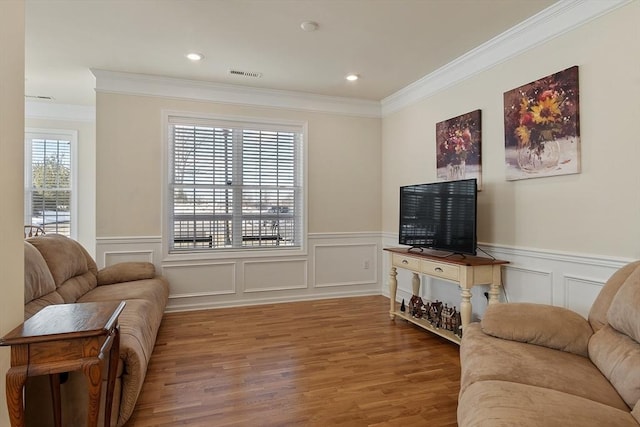 living room featuring ornamental molding, wainscoting, visible vents, and wood finished floors