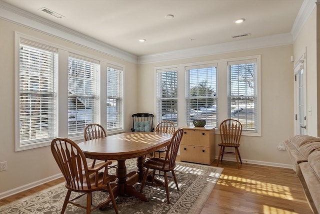 dining area with light wood finished floors, baseboards, visible vents, and ornamental molding