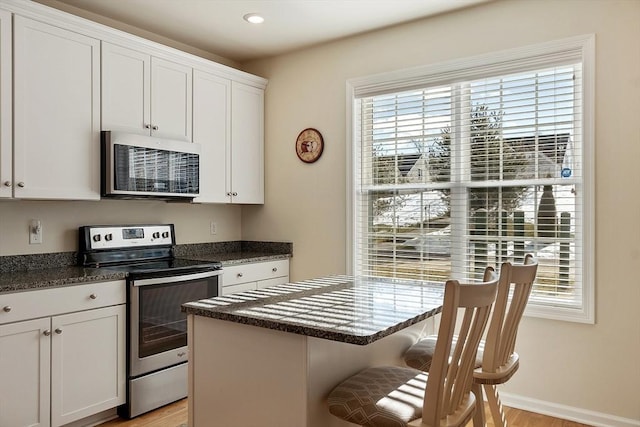 kitchen featuring recessed lighting, white cabinetry, baseboards, stainless steel electric range oven, and a kitchen bar