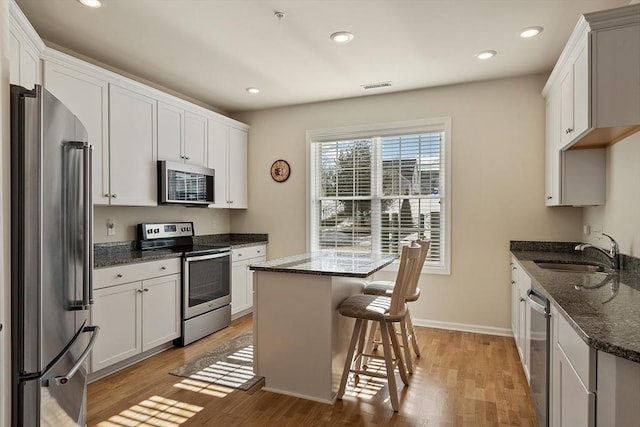 kitchen featuring stainless steel appliances, visible vents, light wood-style floors, a sink, and a kitchen island