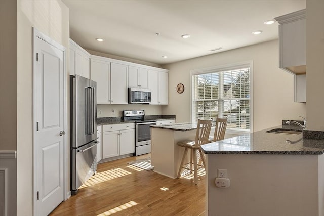 kitchen with light wood finished floors, visible vents, dark stone counters, appliances with stainless steel finishes, and a sink