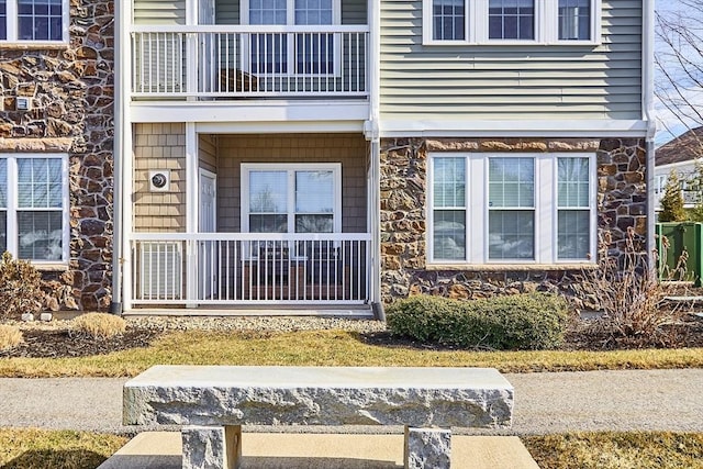 view of exterior entry featuring stone siding and a balcony