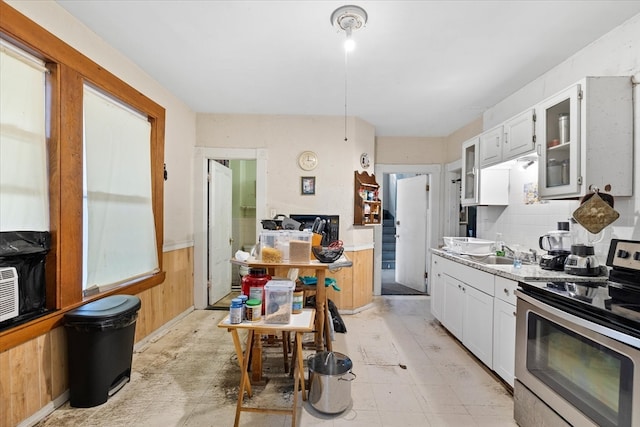 kitchen featuring sink, wooden walls, white cabinetry, and electric stove