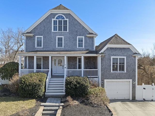 shingle-style home featuring a gate, fence, covered porch, concrete driveway, and an attached garage