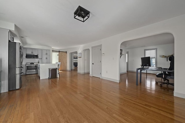 unfurnished living room featuring a barn door, wood finished floors, arched walkways, and baseboards