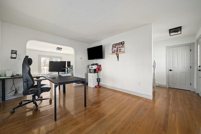 home office with arched walkways, baseboards, and wood finished floors