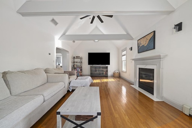 living room featuring wood finished floors, visible vents, vaulted ceiling with beams, arched walkways, and ceiling fan